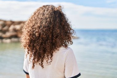Young hispanic woman standing on back view at seaside