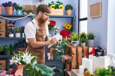 Çiçekçide deftere yazan kızıl saçlı genç bir çiçekçi.