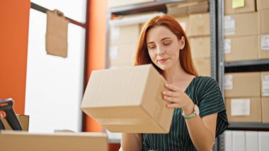 Genç kızıl saçlı kadın, iş kadını. Elinde bir paket var. Masada oturuyor.