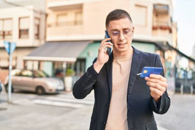 Young hispanic man executive talking on smartphone and credit card at street