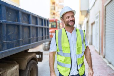 Orta yaşlı mimar sokakta kendine güvenerek gülümsüyor.