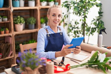 Young blonde woman florist smiling confident using touchpad at florist