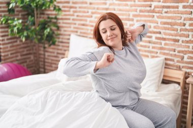 Young beautiful plus size woman waking up stretching arms at bedroom