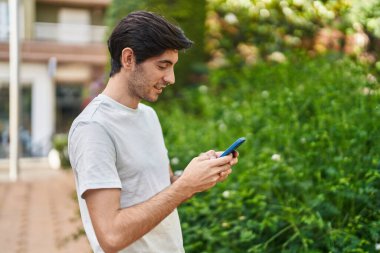 Parkta akıllı telefon kullanarak gülümseyen İspanyol genç adam.