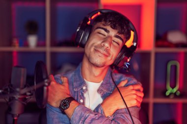 İspanyol asıllı genç bir adam video oyunları oynuyor mutlu ve olumlu bir şekilde kendine sarılıyor, kendinden emin gülümsüyor. Sevgi ve özgüven. 