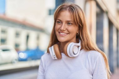 Young blonde girl smiling confident wearing headphones at street