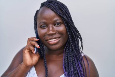 Afro-Amerikalı kadın gülümsüyor. Akıllı telefondan kendine güvenen, izole beyaz arka planda konuşan.