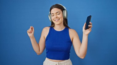 Genç, güzel İspanyol kadın müzik dinliyor ve izole edilmiş mavi arka planda dans ediyor.