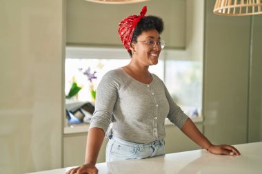 Afro-Amerikalı bir kadın gülümseyerek evde duruyor.