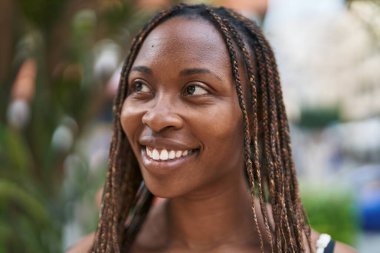 Afro-Amerikalı kadın gülümsüyor. Kendinden emin bir şekilde caddeye bakıyor.