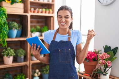 Çiçekçi dükkanında çalışan esmer bir kadın elinde tabletle gururla bağırıyor zaferi ve başarıyı kutluyor. 