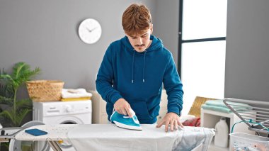 Young hispanic man ironing clothes at laundry room