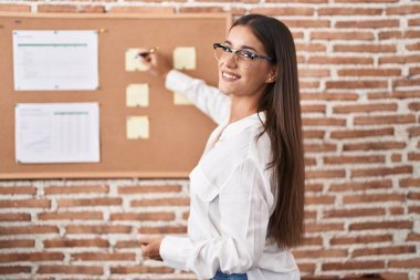 Genç, güzel, İspanyol bir iş adamı ofisteki mantar tahtaya yazı yazıyor.