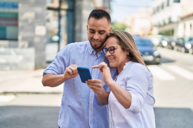 Kadın, erkek, anne ve kız sokakta akıllı telefon kullanıyor.