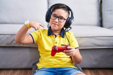 Video oyunu oynayan, kulaklık takan, kendine güvenen, gülümseyen, kendini gururlu ve mutlu gösteren genç İspanyol çocuk.. 