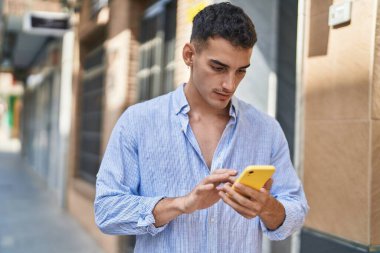 Genç İspanyol adam akıllı telefon kullanıyor. Sokakta ciddi bir ifadesi var.