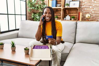 Akıllı telefondan konuşan Afrikalı Amerikalı bir kadın evde online alışveriş için kredi kartı tutuyor.