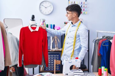 Young hispanic man tailor smiling confident holding t shirt at tailor shop