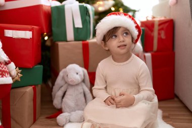 Sevimli kız, kendine güvenerek gülümsüyor Noel ağacının ve hediyelerin yanında oturuyor.