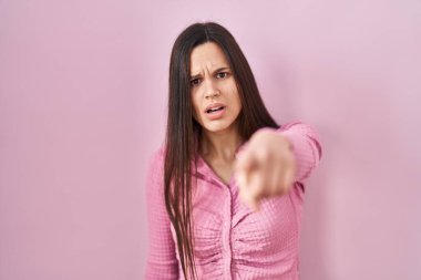 Young hispanic woman standing over pink background pointing displeased and frustrated to the camera, angry and furious with you 