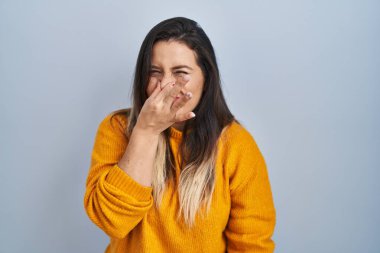 Genç İspanyol kadın izole edilmiş arka planda duruyor. Pis ve iğrenç bir koku alıyor. Nefesini burnunda tutuyor. Kötü kokuyor. 