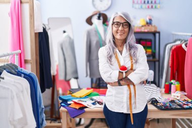 Middle age grey-haired woman tailor smiling confident standing with arms crossed gesture at tailor shop