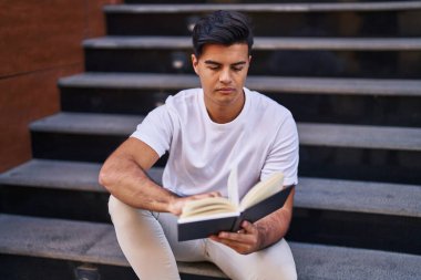 Genç İspanyol adam kitap okuyor. Merdivenlerde oturuyor.