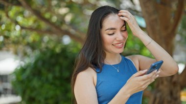 Parkta gülümseyen akıllı telefon kullanan güzel bir İspanyol kadın.