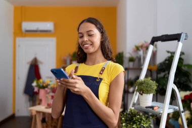 Young african american woman florist smiling confident using smartphone at flower shop