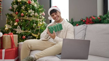 Genç İspanyol adam Noel hediyesini elinde tutarken görüntülü arama yapıyor.