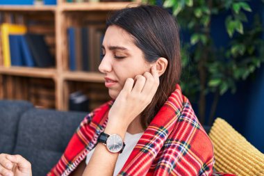 Young beautiful hispanic woman suffering for ear pain sitting on sofa at home