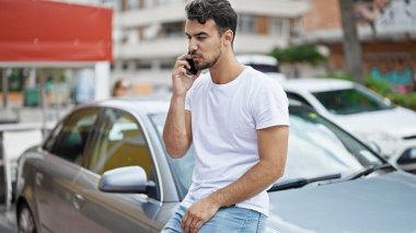 Genç İspanyol adam akıllı telefondan konuşuyor. Sokakta arabada oturuyor.