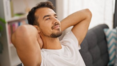 Genç İspanyol adam, ellerini başının üstüne koyup evinde kanepede oturarak rahatladı.