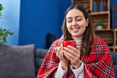 Genç ve güzel İspanyol kadın evdeki kanepede oturup kahve içiyor.