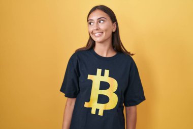 Bitcoin tişörtü giyen genç İspanyol kadın yüzünde gülümsemeyle yan yana bakıyor, doğal bir ifade. Kendinden emin gülen. 