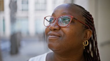 Afro-Amerikan kadın şehir caddesinde duruyor, ciddi bir ifadeyle gökyüzüne bakıyor. Güneş ışığı saçlarına vuruyor, sıradan, büyük boy bir yaşam tarzına uzanıyor..