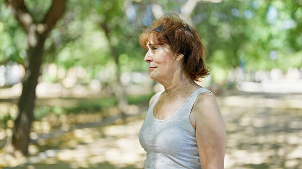 Женщина средних лет смотрит в сторону с серьезным выражением лица в парке
