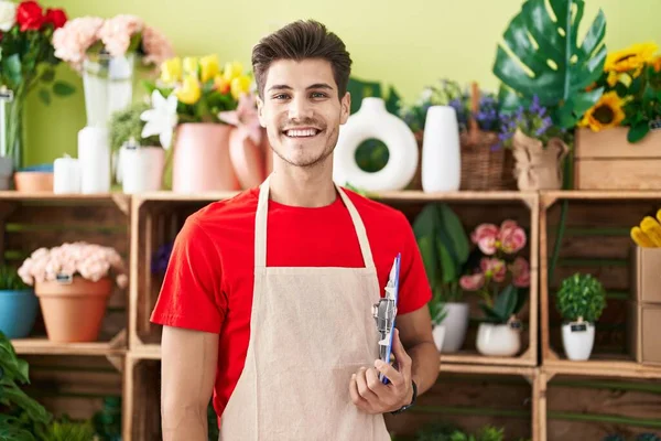 Young hispanic man florist smiling confident holding checklist at flower shop