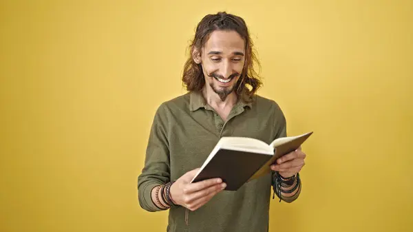 孤立した黄色の背景に微笑む本を読む若いヒスパニックの男 — ストック写真