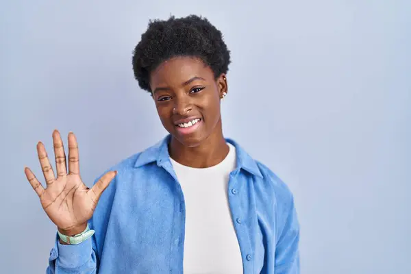 自信を持って幸せな笑顔ながら アフリカ系アメリカ人の女性は青の背景に立って指の数5で見上げと指摘 — ストック写真