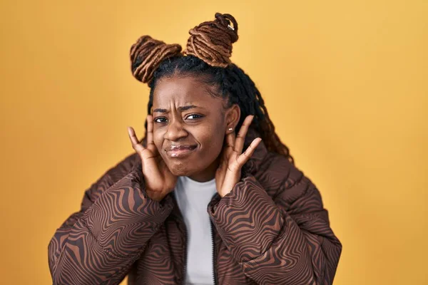 イヤージェスチャーの両手を聞こうとしている黄色の背景の上に立っている編組の髪を持つアフリカの女性 ゴシップに興味があります 聴力の問題 聴覚障害 — ストック写真