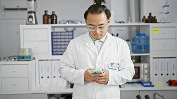 Handsome young chinese man, a passionate scientist in a bustling lab, expertly handling smartphone tech amidst biology research