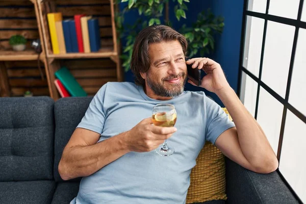 Middle age man talking on the smartphone and drinking wine at home