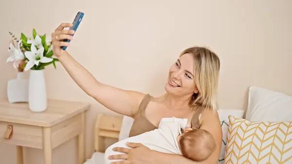 ベッドに座っている母と娘 授乳中の赤ちゃんは 寝室でスマートフォンでセルフィーを作ります — ストック写真