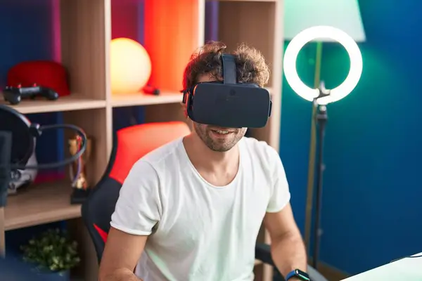 Young hispanic man streamer playing video game using virtual reality glasses at music studio