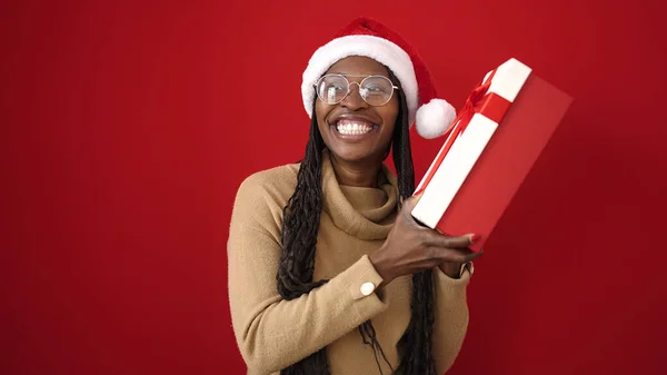 Afrikaanse Vrouw Glimlachen Zelfverzekerd Holding Kerstcadeau Geïsoleerde Rode Achtergrond — Stockfoto