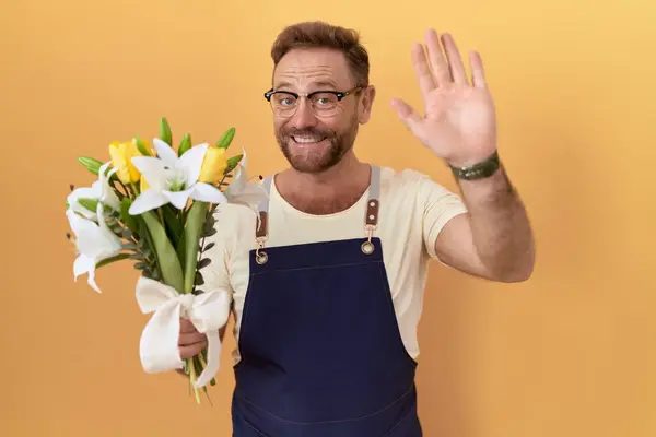 ひげ花屋を持つ中年の男 挨拶を待って花を保持する ハッピーと笑顔 フレンドリーな歓迎のジェスチャー — ストック写真