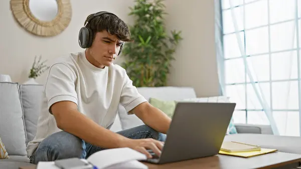 若いヒスパニック系男性学生が自宅で冷静なソファーに座って ノートパソコンを介してオンラインで勉強することに焦点を当て 完全にリラックスしながら ヘッドフォンを介して真剣に知識を浸しながら — ストック写真