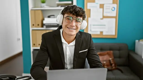 若いヒスパニックビジネスウィズ オフィスでラップトップとヘッドフォンで作業する笑顔のティーンエイジャー — ストック写真