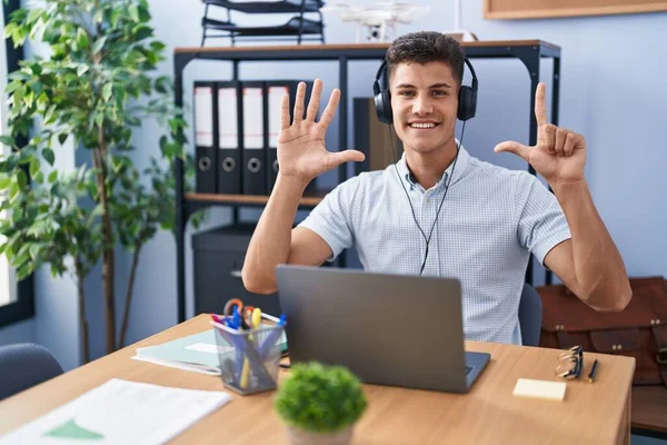 ヘッドフォンを着てオフィスで働く若いヒスパニックの男性は 自信と幸せに微笑んでいる間 指のナンバー7を指で指摘しています — ストック写真